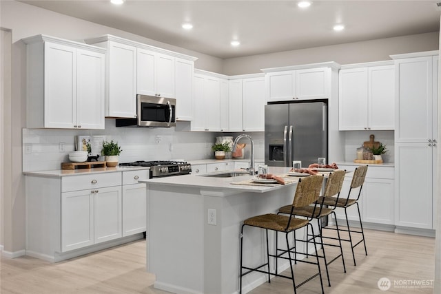 kitchen with a kitchen island with sink, a sink, white cabinets, light countertops, and appliances with stainless steel finishes