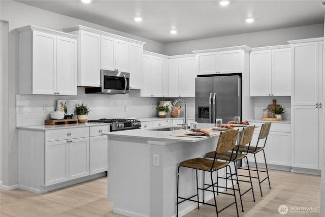 kitchen featuring an island with sink, stainless steel appliances, light countertops, white cabinetry, and a sink