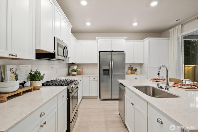 kitchen featuring appliances with stainless steel finishes, white cabinets, a sink, and light stone countertops