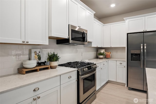 kitchen featuring stainless steel appliances, white cabinets, light wood-type flooring, light stone countertops, and tasteful backsplash