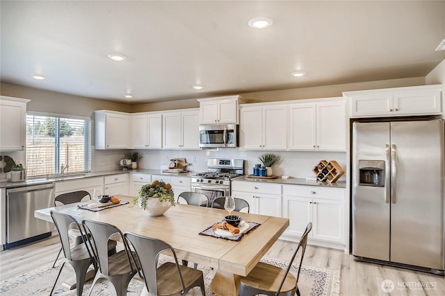 kitchen with light wood finished floors, stainless steel appliances, light countertops, decorative backsplash, and white cabinetry