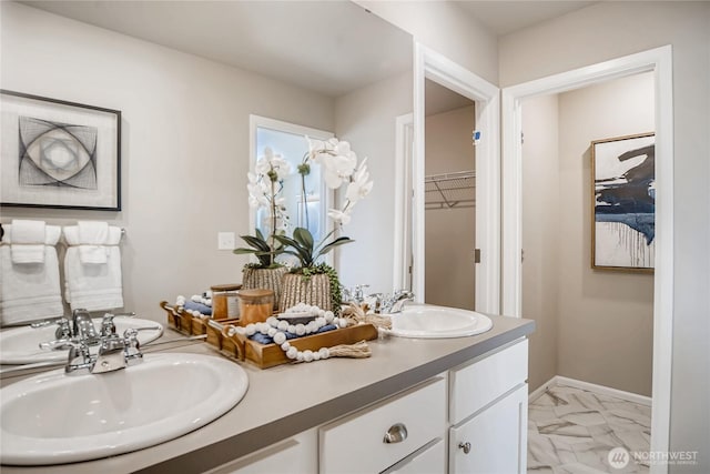 full bath featuring double vanity, marble finish floor, a spacious closet, and a sink