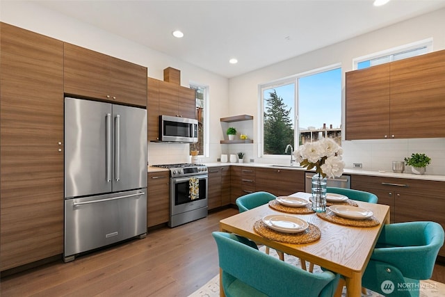 kitchen with light wood finished floors, open shelves, decorative backsplash, appliances with stainless steel finishes, and modern cabinets