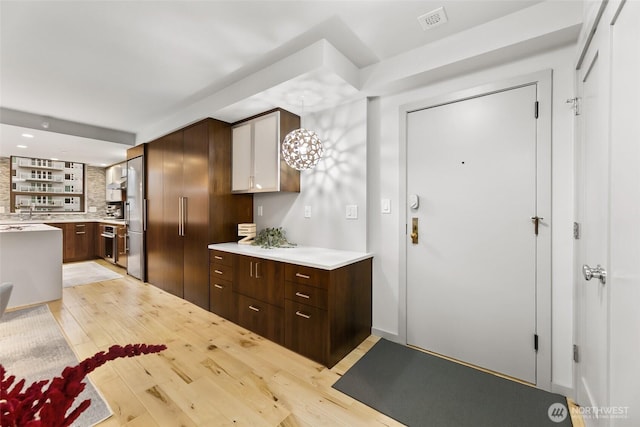 kitchen featuring light wood finished floors, light countertops, hanging light fixtures, visible vents, and oven