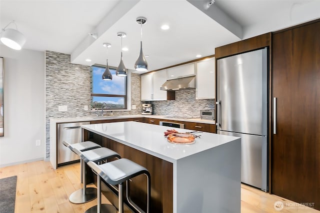 kitchen featuring exhaust hood, white cabinets, light countertops, appliances with stainless steel finishes, and decorative light fixtures