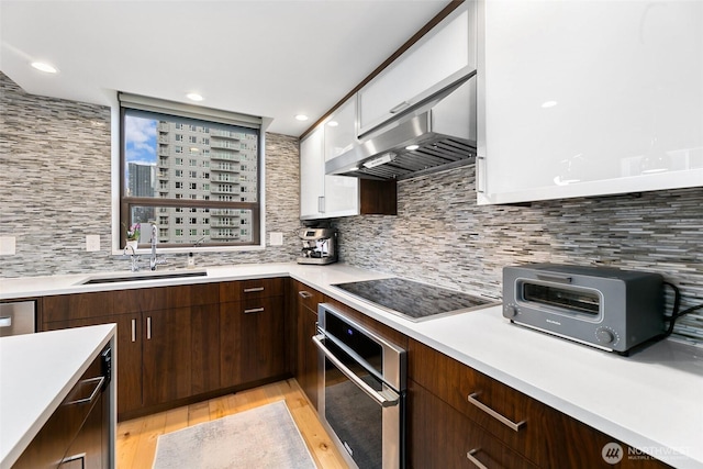 kitchen with white cabinets, black electric cooktop, light countertops, stainless steel oven, and a sink