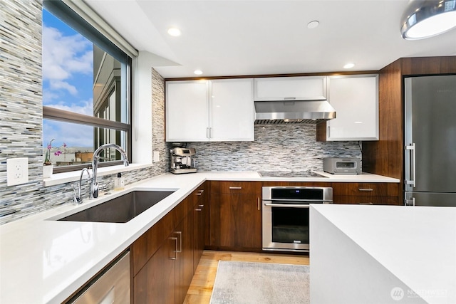 kitchen with white cabinets, appliances with stainless steel finishes, light countertops, a sink, and exhaust hood