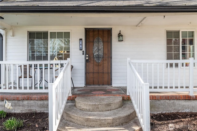 view of exterior entry with covered porch and a shingled roof