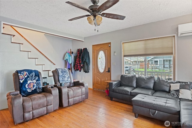 living area with a wall unit AC, ceiling fan, stairway, hardwood / wood-style floors, and a textured ceiling