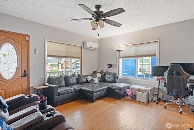 living area with a textured ceiling, ceiling fan, a wall unit AC, and hardwood / wood-style flooring