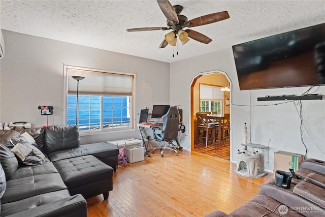 living area featuring a wealth of natural light, arched walkways, hardwood / wood-style floors, and a ceiling fan