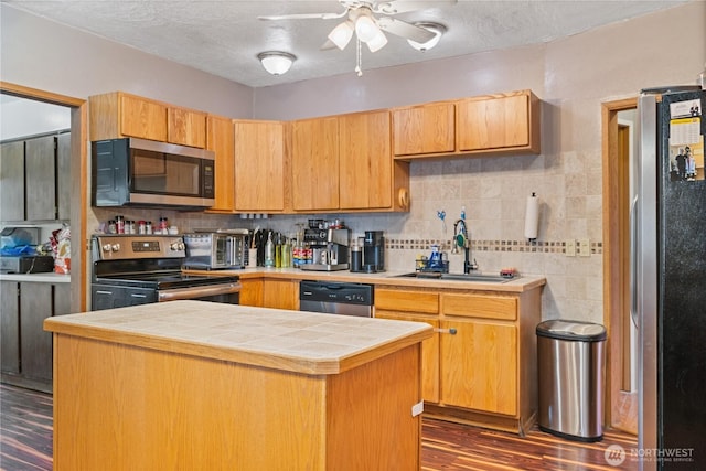 kitchen with tile countertops, stainless steel appliances, a sink, a center island, and dark wood finished floors