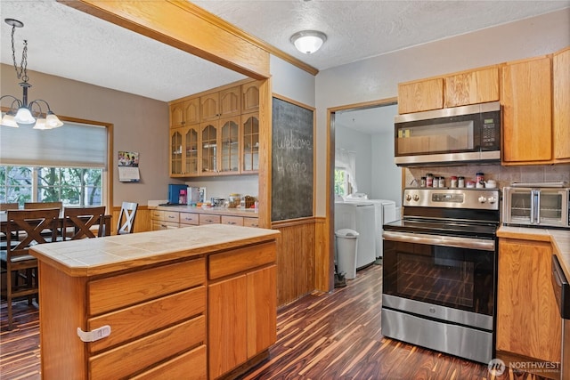 kitchen with tile countertops, a chandelier, dark wood-type flooring, washer and dryer, and appliances with stainless steel finishes