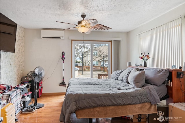 bedroom featuring a wall unit AC, ceiling fan, light wood-style flooring, access to outside, and a textured ceiling