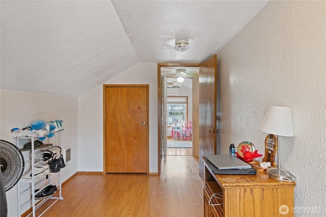 interior space featuring lofted ceiling, a textured wall, light wood-style flooring, a textured ceiling, and baseboards