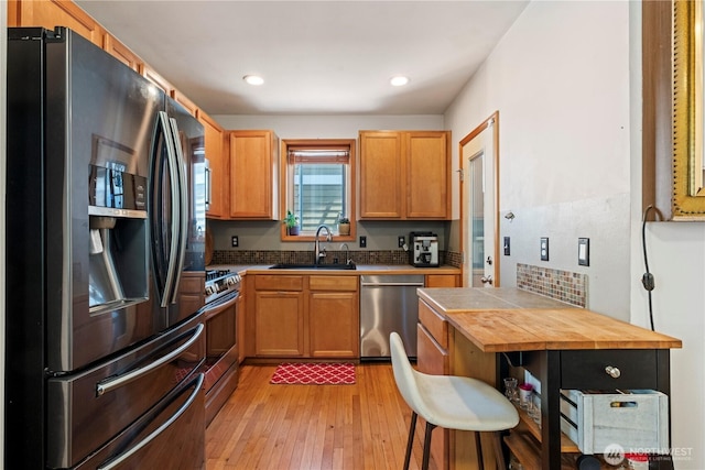 kitchen featuring brown cabinetry, appliances with stainless steel finishes, light wood-type flooring, a sink, and recessed lighting