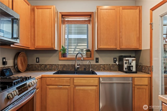 kitchen featuring stainless steel appliances, a sink, tile countertops, and decorative backsplash