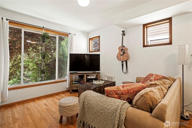 living area featuring plenty of natural light, wood-type flooring, visible vents, and baseboards