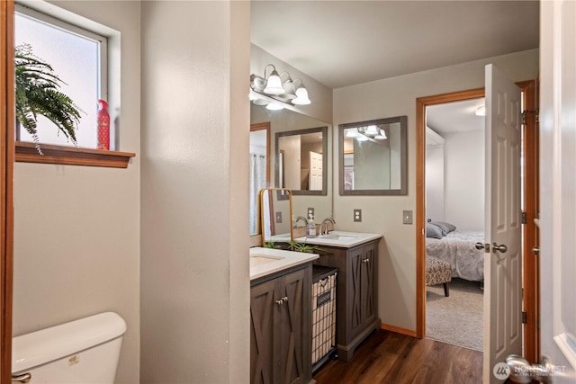 bathroom with toilet, connected bathroom, vanity, wood finished floors, and baseboards