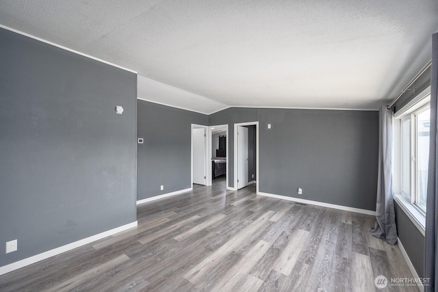 spare room featuring lofted ceiling, a textured ceiling, baseboards, and wood finished floors