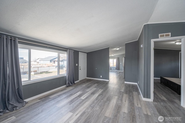 spare room with a textured ceiling, lofted ceiling, wood finished floors, visible vents, and baseboards