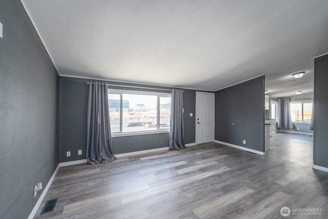 spare room with baseboards, visible vents, a textured wall, wood finished floors, and a textured ceiling