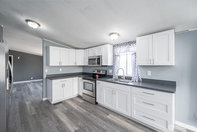 kitchen with dark countertops, white cabinets, stainless steel appliances, and a sink