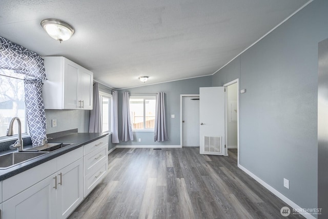 kitchen with a sink, visible vents, white cabinetry, vaulted ceiling, and dark countertops