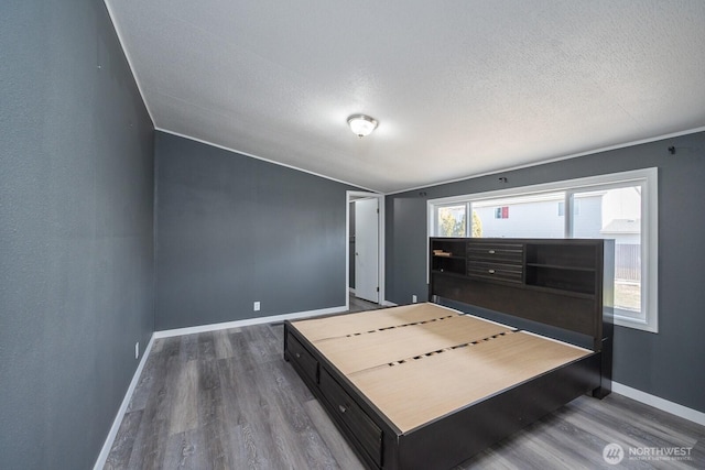 unfurnished bedroom with a textured ceiling, wood finished floors, and baseboards