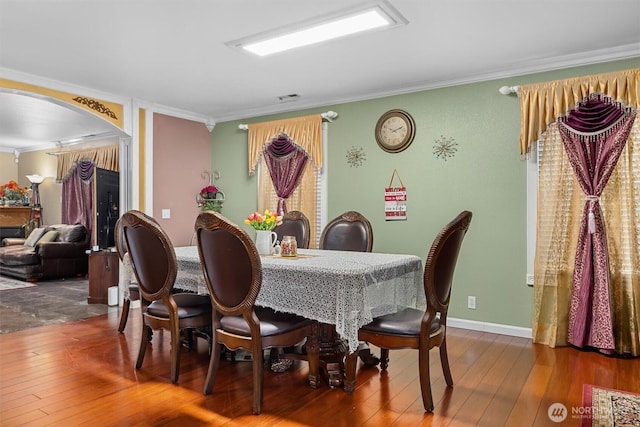 dining space featuring arched walkways, visible vents, hardwood / wood-style floors, ornamental molding, and baseboards