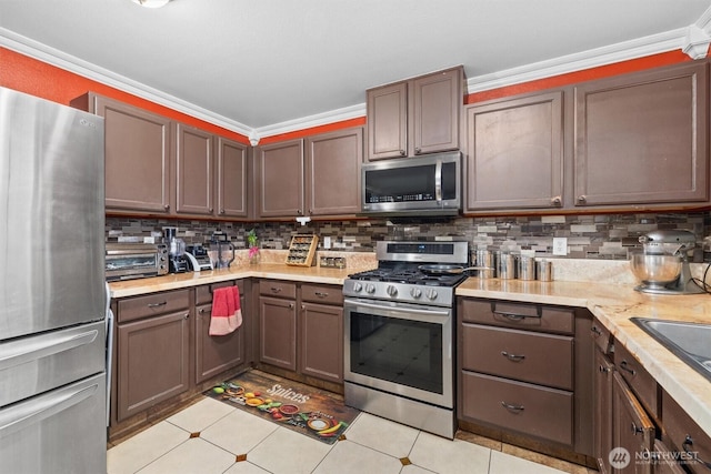 kitchen featuring appliances with stainless steel finishes, light countertops, crown molding, and backsplash