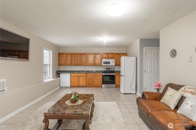 kitchen featuring light tile patterned floors, white appliances, a sink, baseboards, and dark countertops