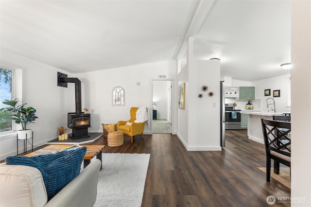 living area with vaulted ceiling, a wood stove, dark wood finished floors, and baseboards