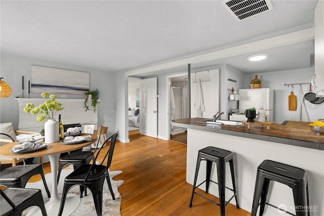 kitchen featuring a breakfast bar area, visible vents, freestanding refrigerator, a sink, and wood finished floors