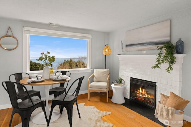 dining space with a brick fireplace, visible vents, baseboards, and wood finished floors