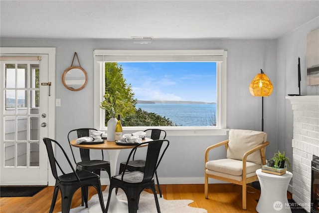 dining room with a water view, a fireplace, light wood-style flooring, and baseboards