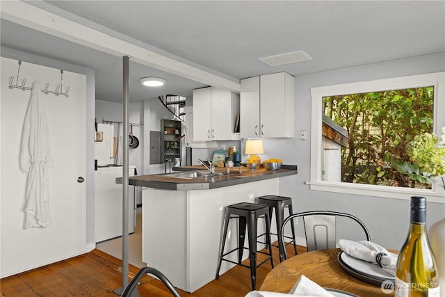 kitchen featuring a breakfast bar, dark wood-style flooring, dark countertops, white cabinetry, and a sink