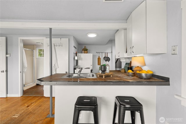 kitchen with dark countertops, a breakfast bar area, white cabinets, and a sink