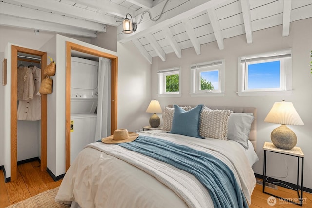 bedroom featuring lofted ceiling with beams, stacked washer / dryer, visible vents, baseboards, and light wood-type flooring