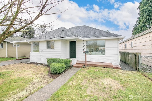 bungalow featuring roof with shingles, fence, and a front lawn