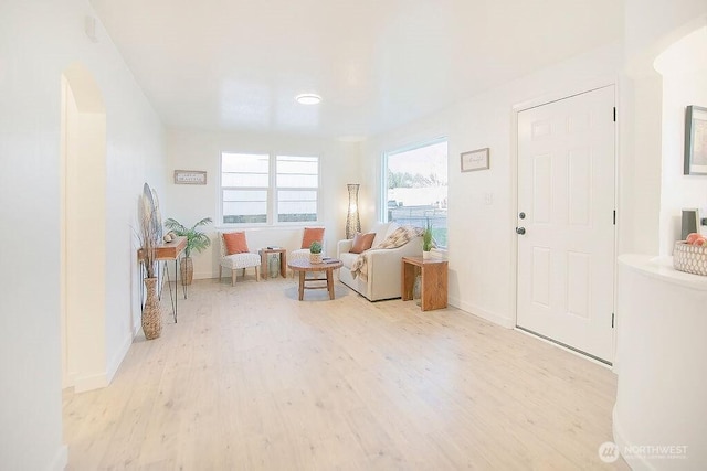 sitting room with arched walkways, light wood-style flooring, and baseboards