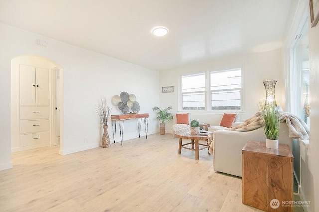 sitting room featuring arched walkways, baseboards, and light wood-style floors