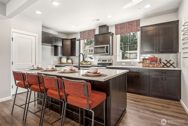 kitchen featuring a breakfast bar area, dark wood-type flooring, light countertops, appliances with stainless steel finishes, and an island with sink