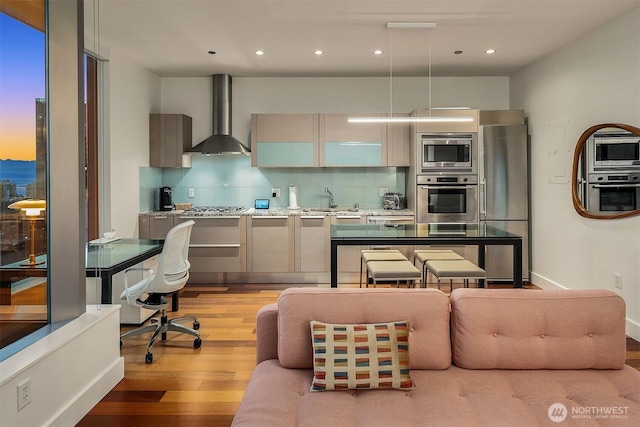 kitchen with light wood-style flooring, appliances with stainless steel finishes, decorative backsplash, wall chimney exhaust hood, and modern cabinets