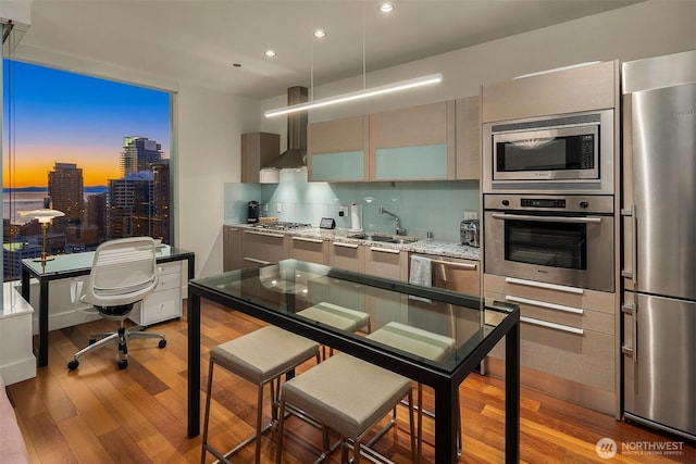 kitchen with a city view, appliances with stainless steel finishes, a sink, wall chimney range hood, and light wood-type flooring