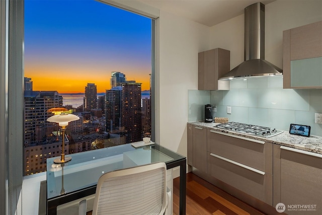 kitchen with wall chimney range hood, a view of city, stainless steel gas cooktop, and gray cabinetry