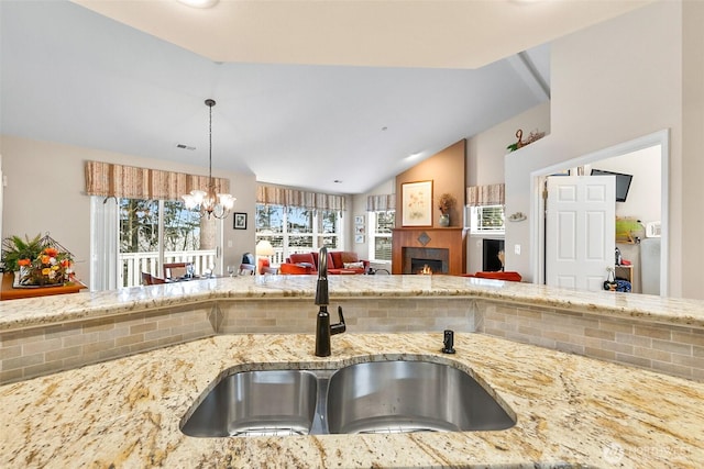 kitchen featuring pendant lighting, lofted ceiling, a tiled fireplace, open floor plan, and a sink