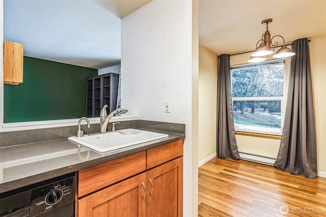 kitchen with black dishwasher, dark countertops, decorative light fixtures, light wood-type flooring, and a sink