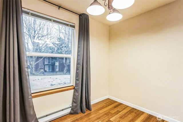 empty room featuring a baseboard radiator, wood finished floors, and baseboards