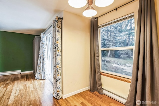 spare room featuring a baseboard heating unit, baseboards, and wood finished floors